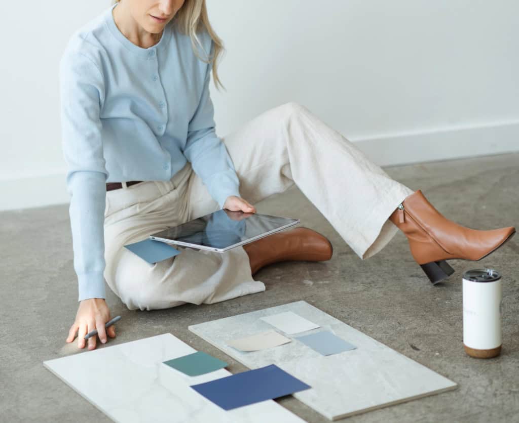 Ricki-Lee from North Pacific Homes Group using a tablet while reviewing flooring and design samples laid out in front of her during a new construction consultation in Victoria, BC.