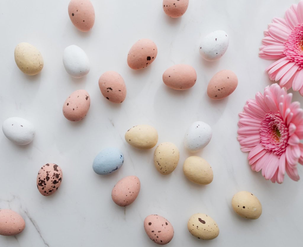 Speckled eggs on a marble countertop with pink flowers in the corner,