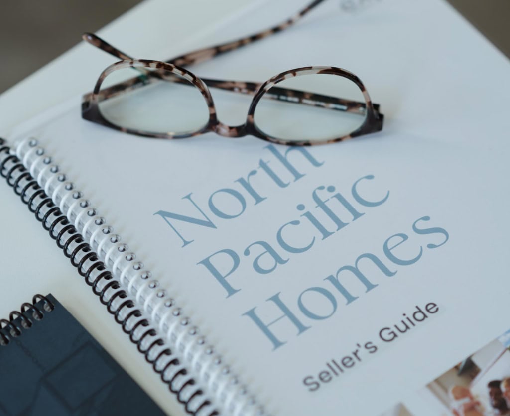 Resource for sellers by the North Pacific Homes Group with eXp Realty in Greater Victoria, BC, a coil-bound guide, and a pair of glasses on a desk.