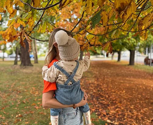 A mom and toddler stand on a path covered in leaves in Victoria, BC.
