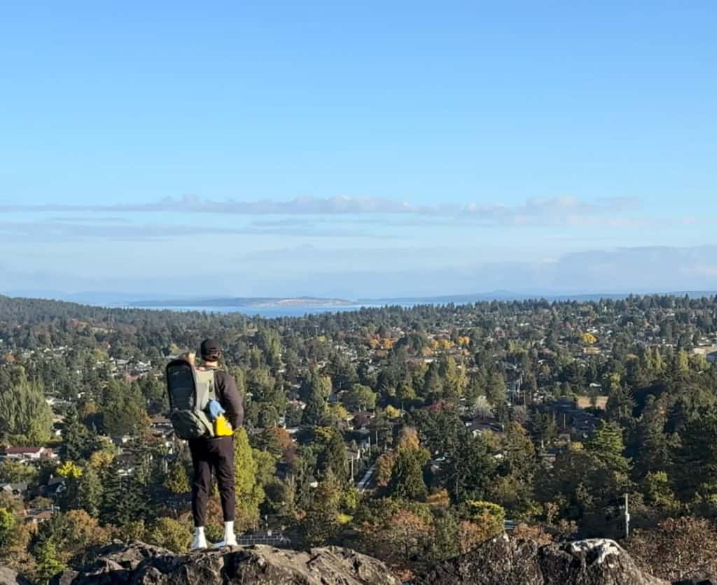Alex standing at a lookout point above Greater Victoria, BC with a hiking backpack carrying his toddler.